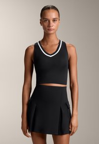 Črn kroj majice s V-izrezom in belimi črtami, kombiniran s črno nabranico s stranskimi žepi. Gladka tekstura po celotni površini.