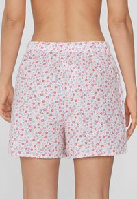 Kraťasy s květinovým vzorem na pastelově růžovém pozadí. Materiál je lehký a má volný střih, s elastickým pasem.
