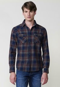 Camicia a maniche lunghe a quadri in blu navy, rosso e crema. Presenta due tasche sul petto, colletto con bottoni e orlo curvo. Tessuto morbido.