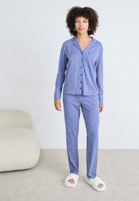 Blå och rosa randig pyjamas med en knäpp skjorta och åtsittande byxor, kombinerad med vita fluffiga tofflor. Mjuk tygtextur.
