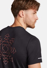 Black t-shirt featuring a geometric orange pattern on the back, round neckline, short sleeves, and reflective accents on the shoulder.