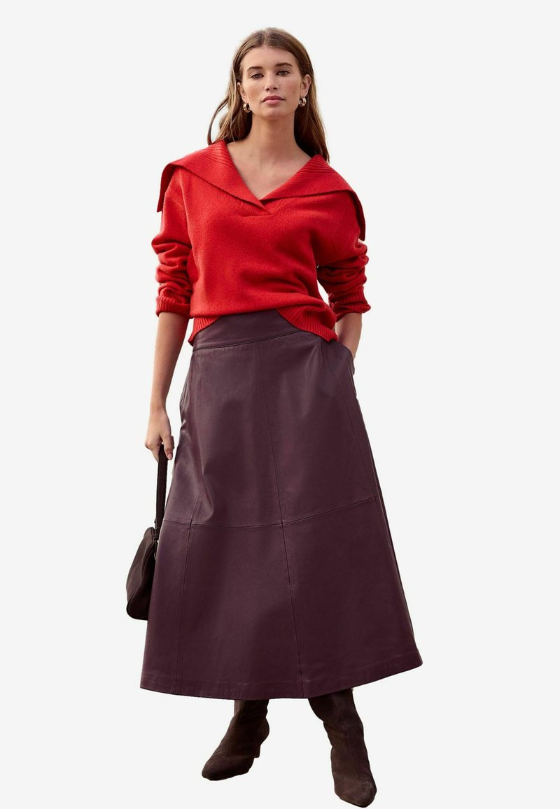 Red oversized sweater with a wide collar, paired with a long purple leather skirt. Model holds a brown handbag and wears brown ankle boots.