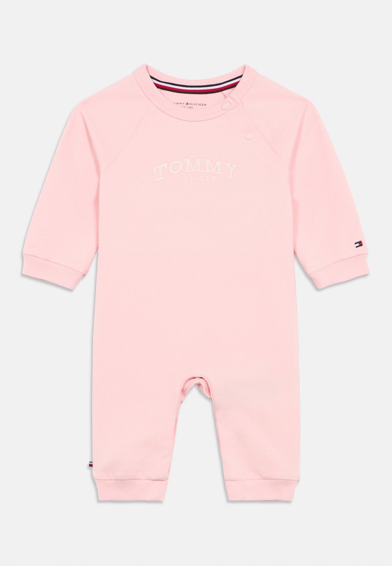 Salopetă pentru bebeluși de culoare roz deschis, fabricată dintr-un material moale, având guler rotund, mâneci lungi și logo-ul brodat "TOMMY HILFIGER" pe față.