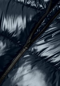 Gros plan d'un tissu matelassé bleu foncé brillant avec une fermeture éclair noire partiellement ouverte qui court verticalement.