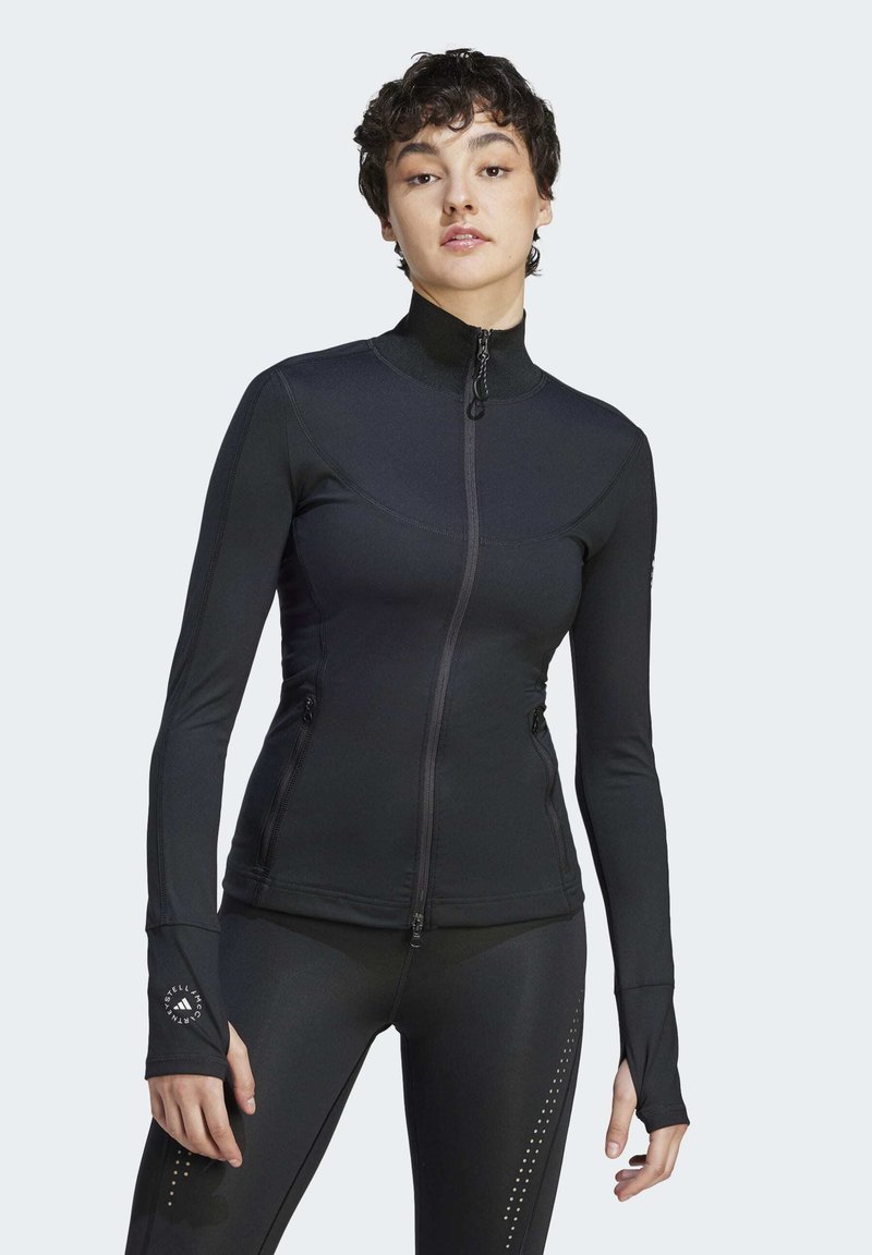 Chaqueta negra ajustada con cremallera, hecha de material elástico, de manga larga, con cuello alto, que cuenta con bolsillos laterales y orificios para los pulgares en los puños.