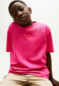 Różowa bawełniana koszulka z okrągłym dekoltem i krótkimi rękawami, z subtelnym haftem na piersiach. Gładka tekstura.