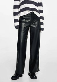 Černé kalhoty z umělé kůže v širokém střihu s předními kapsami a prošívanými detaily, spárované s pleteným svetrem bílého a námořnického pruhu.