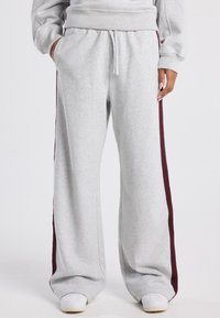Graue Sweatpants aus weichem Stoff mit einer lässigen Passform, elastischem Bund und burgunderroten Seitenstreifen für einen Kontrast.