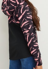 Hoodiejacka med en svart bas och rosa penseldragsmönster på ärmarna och överkroppen, tillverkad av ett slätt, stretchigt tyg.