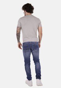 Camiseta ajustada de color gris claro, de manga corta, combinada con jeans ajustados de color azul oscuro, con dos bolsillos traseros y zapatillas blancas.