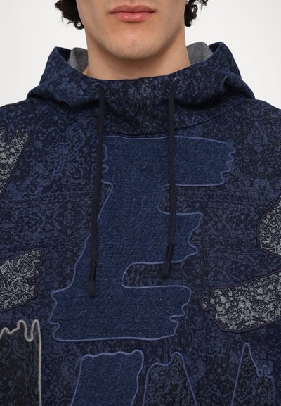 Le sweat à capuche bleu marine présente un motif texturé, un grand design brodé et des accents à cordon sur la capuche.