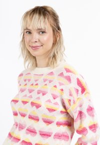 Strickpullover mit einem cremigen Grundton und einem bunten Herzmuster in Rosatönen und Gelb. Runder Ausschnitt, strukturiertes Gewebe, lockere Passform.