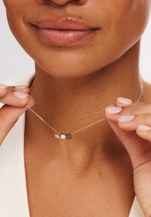 Collier doré avec trois charms : une étoile, un cœur et un cube, dont un est orné d'une pierre précieuse claire.