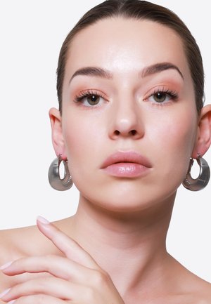 Les boucles d'oreilles en argent sont ornées d'un design texturé avec une forme circulaire ouverte. Elles ont une finition polie et une légère brillance réfléchissante.