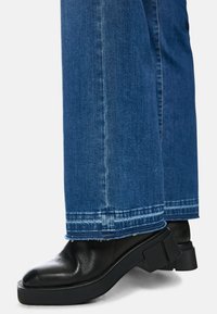 Black leather ankle boots with thick, textured soles paired with blue denim flared jeans featuring frayed hem and contrasting stitching details.
