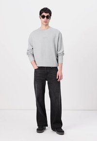 Gray sweatshirt with a textured appearance, paired with loose black jeans and black sneakers. Model wears dark sunglasses.
