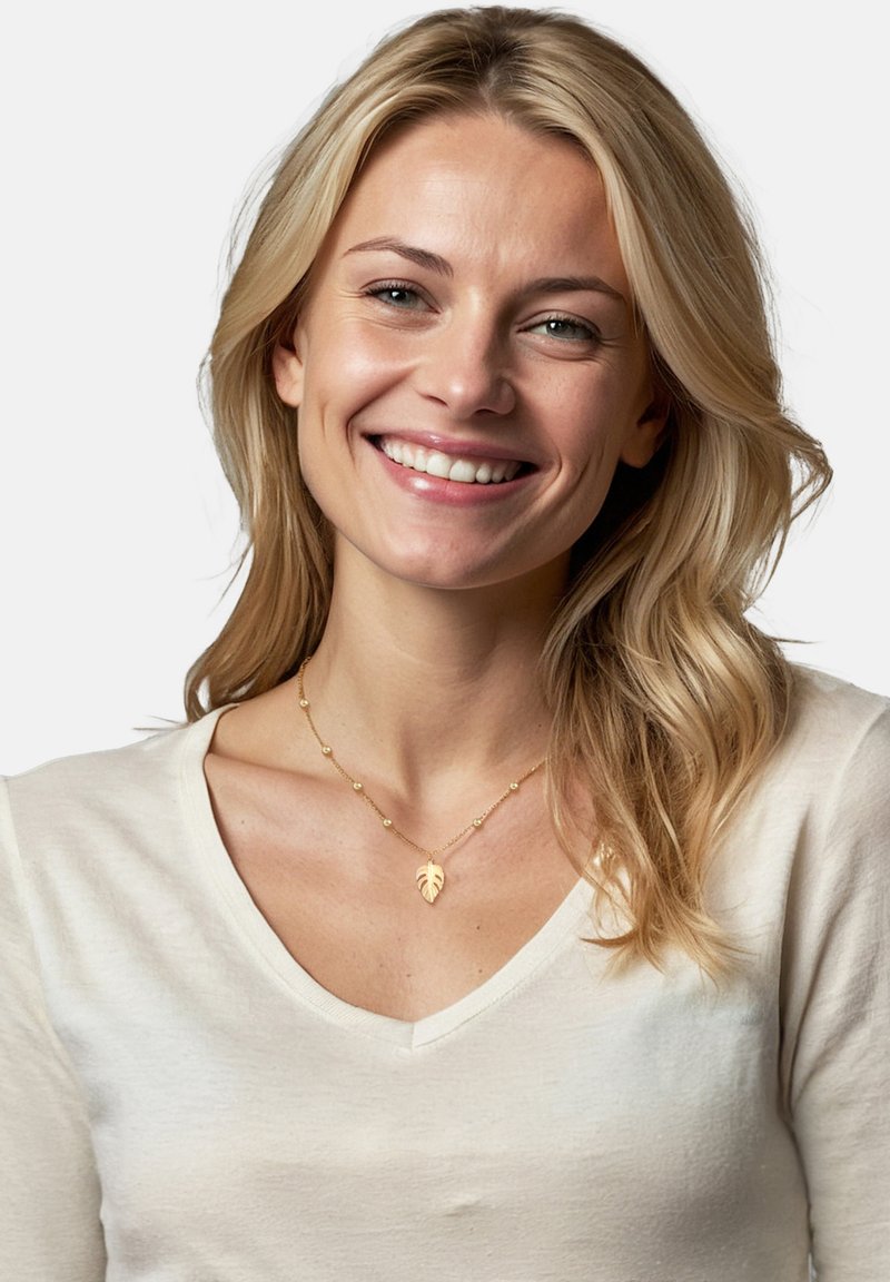 Guldbladspend med en delikat kedja och små cirkulära detaljer, bärs över en ljusbeige V-ringad topp. Slät textur, elegant design.