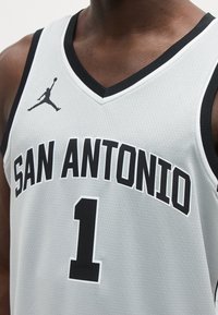 Άνδρας που φοράει λευκή φανέλα μπάσκετ της San Antonio με μαύρο περίγραμμα, αριθμό 1 και λογότυπο Jumpman στο στήθος.