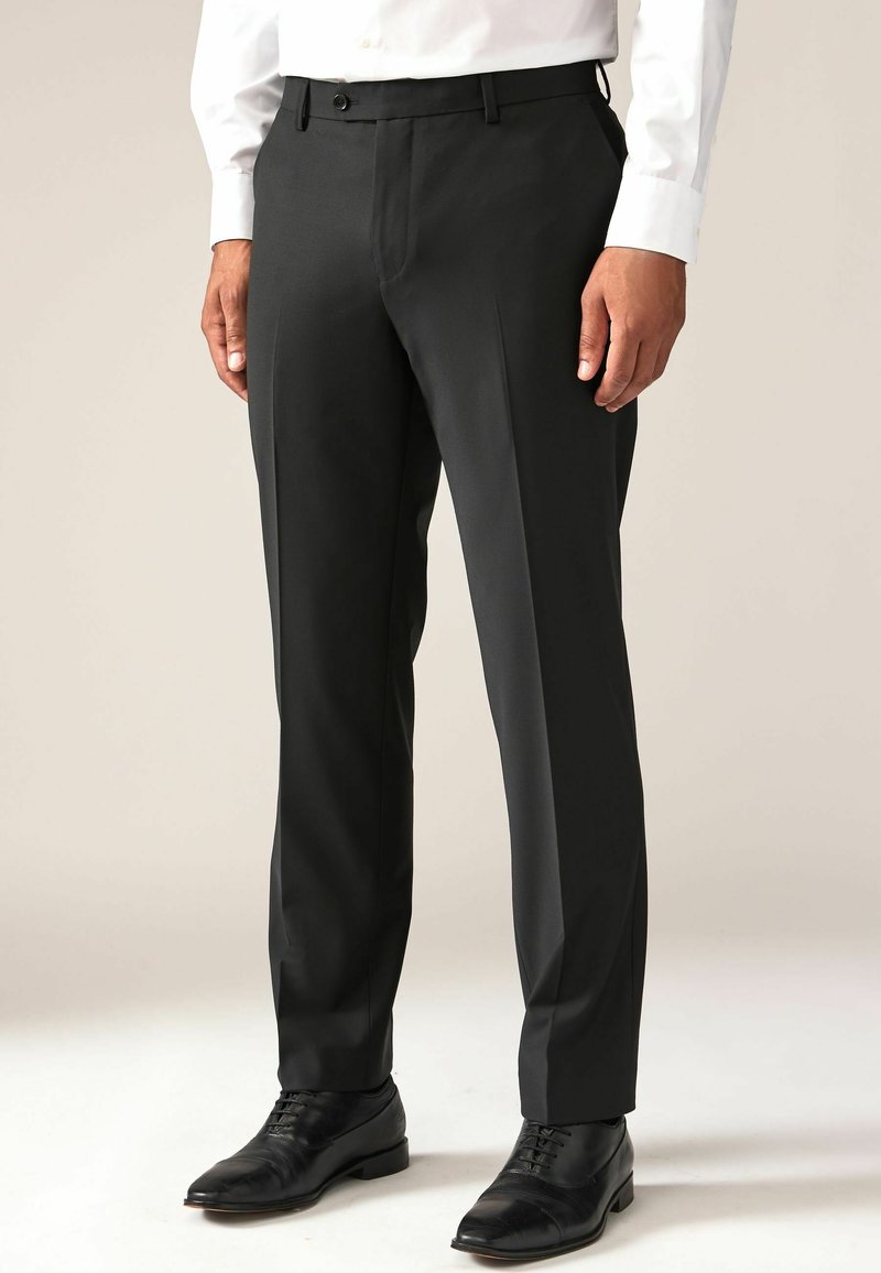 Sorte dressbukser med slim fit, glat tekstur og flad front. Har sidelommer og en enkelt knaplukning. Bæres med sorte dresssko.