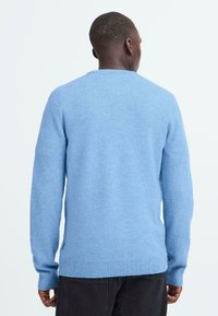 Pull en tricot bleu clair, à manches longues et col rond. Le tissu semble doux ; il présente des poignets et une taille côtelés. Design simple, sans motifs.