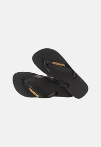 Black rubber flip-flops with textured soles and black straps featuring small gold "Havaianas" logos on the outer sides.