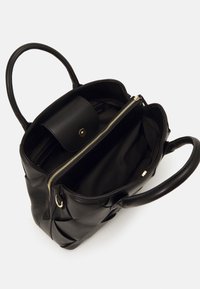 Svart läderhandväska med två handtag. Har dragkedjor, ett avtagbart fickstängningssystem och slät inredning. Kuddad, vadderad textur.