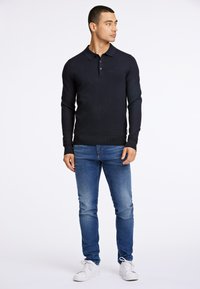 Navy pitkähihaista polo-paitaa, joka on valmistettu ribbatusta puuvillasta, varustettuna kauluksella, kolmella napilla ja yhdistettynä vaaleansinisiin farkkuihin sekä valkoisiin tennareihin.