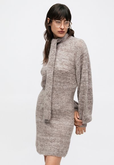 Pletené šaty v tlmenom taupe odtieni s jemným, textúrovaným povrchom, vybavené vysokým výstrihom a viazaním na golieri, s dlhými, objemnými rukávmi.