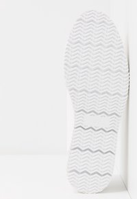 Vit sneakersula med zigzagmönster, slät textur och märkning "37" prägling på sidan, vinklad mot en ljus bakgrund.