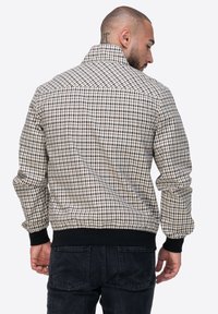 Męska marynarka w kratę w beżowym, brązowym i czarnym kolorze. Posiada kołnierz stojący, elastyczne mankiety oraz pas. Wykonana z lekkiego materiału o gładkiej teksturze.