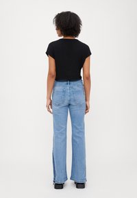 T-shirt nera cropped abbinata a jeans svasati di un leggero blu, con dettagli a fessura laterale. Tessuto morbido, vestibilità casual e design basico.