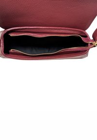 Otwarta bordowa skórzana torebka z złotym zamkiem, ukazująca pustą czarną wnętrze i teksturowaną powierzchnię zewnętrzną.