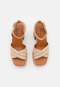 Woven beige strap sandals with a square toe, brown vegan leather insole, and a short cork heel. Buckle closure on the ankle strap.