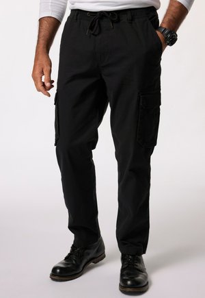 Zwarte cargobroek met elastische tailleband en trekkoord. Bevat zijzakken en heeft een relaxte pasvorm. Draagt met zwarte leren schoenen.