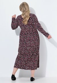 Langärmliges, florales Kleid mit einem dunkelroten Hintergrund, das mit kleinen weißen und grünen Blumen verziert ist. Die langen Ärmel haben einen fließenden, lockeren Schnitt. Schwarze Schuhe.