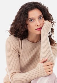 Beiger, gerippter Strickpullover mit langen Ärmeln und Daumenlöchern. Weiche Textur, runder Ausschnitt, figurbetontes Design mit subtilen vertikalen Linien.