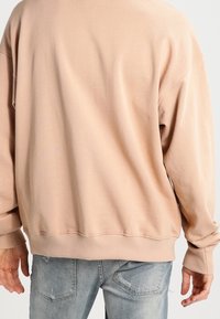 Felpa oversized beige chiaro con polsini e orlo a coste; realizzata in tessuto morbido. Indossata con jeans azzurri strappati.