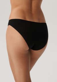 Czarne majtki bikini o gładkiej tkaninie, minimalistycznym kroju, wysokich wycięciach na nogawki oraz czystych szwach dla uzyskania bezszwowego wyglądu.