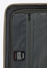 Black suitcase interior featuring gray fabric, mesh compartments, a label, and subtle airplane pattern, with a zipper and textures for organization.