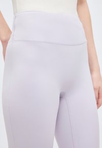 Κοντινό πλάνο ατόμου που φοράει ψηλόμεσα, εφαρμοστά κολάν σε ανοιχτό λεβαντίνι με εμφανείς ραφές.