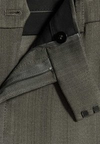 Gros plan d'une veste grise sur mesure montrant le col, le bouton et les détails du tissu texturé.