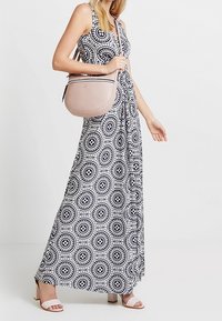 Maxi sukienka w czerni i bieli z okrągłymi wzorami, połączona z jasnoróżową torebką na ramię i białymi sandałami na słupkowym obcasie.