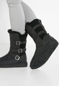 Bottes cheville en daim noir et textile avec détails à boucles, hauts doublés de fourrure et semelles en caoutchouc texturé. Dotées d'un talon plat et d'un bout arrondi.