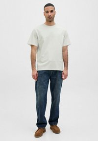 Lichtgrijs katoenen t-shirt met een relaxte pasvorm, korte mouwen en een ronde hals, gecombineerd met donkerblauwe spijkerbroek en bruine loafers.
