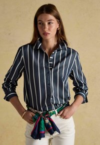 Tumesinise ja valgete triipudega nööbiga särk, pikad varrukad üles keeratud, koos rohelise ja mustrilise sallivöödiga. Sile kangastruktuur.