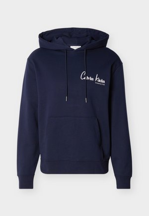 Mørkeblå hettegenser med kengurulomme foran, snøring i hette, og hvit "Calvin Klein Established 1968"-logo på brystet.