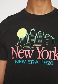 Svart t-shirt med livlig grafisk design som visar en stadssiluett, en gul sol, en gul taxi och texten "New York NEW ERA 1920" i rosa och blått.