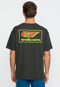 T-shirt noir à manches courtes avec un grand logo Volcom rouge et vert au dos, fabriqué en coton avec une coupe décontractée.