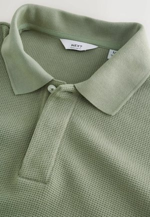 Poloshirt in Hellgrün, gefertigt aus strukturiertem Stoff mit Kragen, zwei Knöpfen und sichtbaren Etiketten am Kragen.