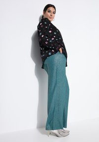 Blouse noire à pois colorés, associée à un pantalon large en teal chatoyant et des bottes à talons métalliques argentées.